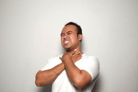 Asian man wearing white T Shirt, isolated white background, Sore throat, shouting suffocate because...