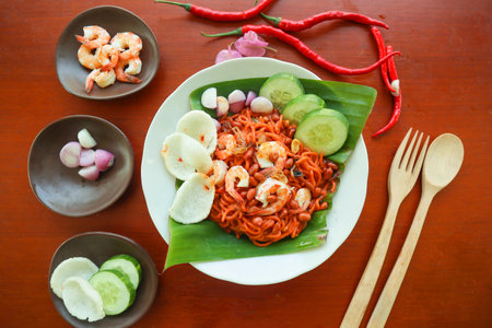 Mi Aceh, Mie Aceh or Acehnese noodles is a spicy dish typical of Aceh consisting of thick yellow noodles, slices of beef, mutton or shrimp, sliced ââred onions, cucumbers with a savory and spicy curry sauce. on tableの写真素材