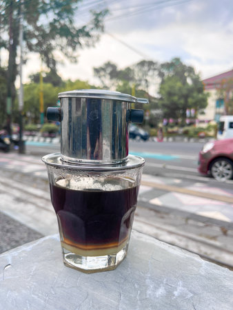 Vietnamese drip, Vietnamese coffee with condensed milk in glass cups and traditional metal coffee maker phin. Traditional method of making of vietnamese coffee. served on outdoorの写真素材