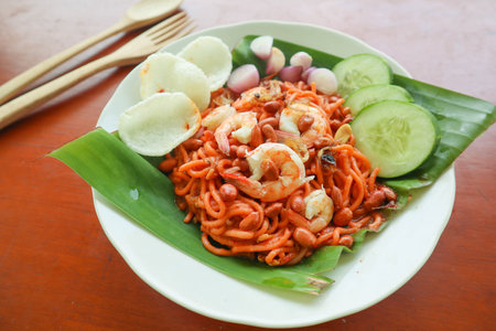 Mi Aceh, Mie Aceh or Acehnese noodles is a spicy dish typical of Aceh consisting of thick yellow noodles, slices of beef, mutton or shrimp, sliced ââred onions, cucumbers with a savory and spicy curry sauce. on tableの写真素材