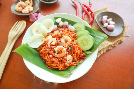 Mi Aceh, Mie Aceh or Acehnese noodles is a spicy dish typical of Aceh consisting of thick yellow noodles, slices of beef, mutton or shrimp, sliced ââred onions, cucumbers with a savory and spicy curry sauce. on tableの写真素材