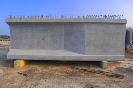 Prestressed concrete or Three gray concrete blocks are stacked on top of each other. The blocks are in a field and are surrounded by a green machineの写真素材