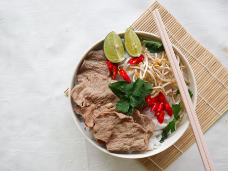 A Bowl Pho Bo traditional Soup with beef, rice noodles, ginger, lime, chili pepper in bowl. Close...