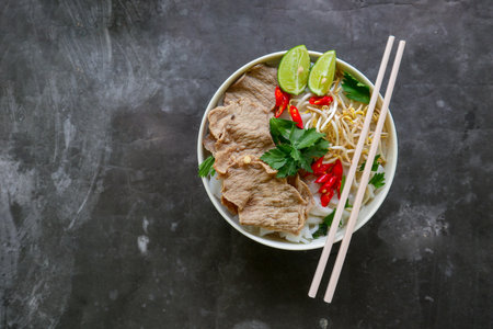 A Bowl Pho Bo traditional Soup with beef, rice noodles, ginger, lime, chili pepper in bowl. Close...