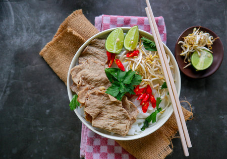 A Bowl Pho Bo traditional Soup with beef, rice noodles, ginger, lime, chili pepper in bowl. Close up. Vietnamese cuisine served on black backgroundの写真素材
