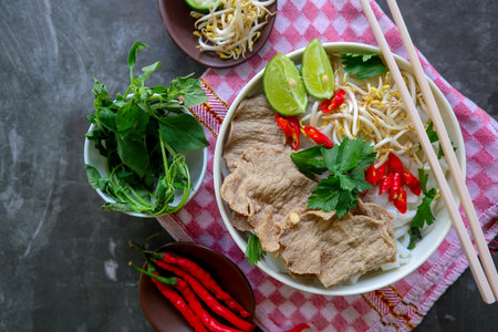 A Bowl Pho Bo traditional Soup with beef, rice noodles, ginger, lime, chili pepper in bowl. Close...