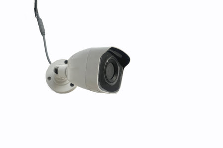 A camera CCTV is hanging from a cord. The camera is white and black, isolated on white background