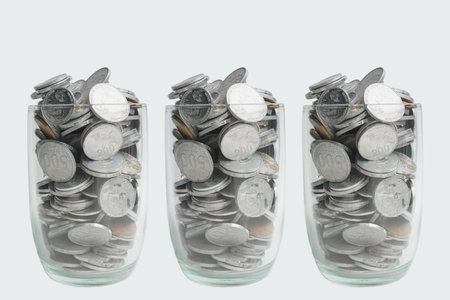 Three glass filled with silver rupiah coins, on white background