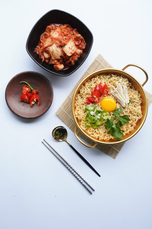 Ramyeon or Ramyun is Korean instant noodle, with spicy flavour topped with egg yolk, chilli, mushroom, kimchi inside a traditional korean noodle pot. Serving a Korean styleの写真素材