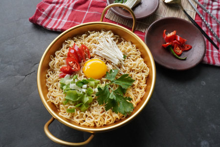 Ramyeon or Ramyun is Korean instant noodle, with spicy flavour topped with egg yolk, chilli, mushroom, kimchi inside a traditional korean noodle pot. Serving a Korean styleの写真素材