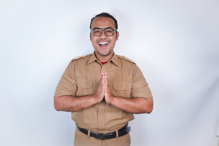 a man Asian civil servants or state civil servants is with brown uniform gesturing traditional greeting On white background. Indonesia PNS, ASNの写真素材
