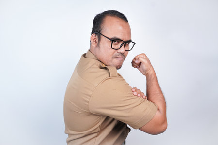 a man Asian civil servants or state civil servants is with brown uniform. gesture showing strong gesture by lifting his arms and muscles smiling proudly. On white background. Indonesia PNS, ASNの写真素材
