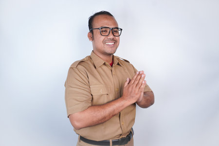a man Asian civil servants or state civil servants is with brown uniform gesturing traditional greeting On white background. Indonesia PNS, ASNの写真素材
