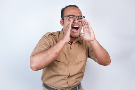 a man Asian civil servants or state civil servants is with brown uniform. gesture shouting and screaming loud with a hand on her mouth. On white background. Indonesia PNS, ASNの写真素材