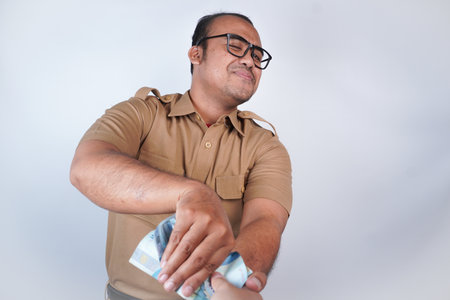 a man Asian civil servants or state civil servants is with brown uniform. gesturing take bribes. money, taking bribe from man under table. On white background. Indonesia PNS, ASNの写真素材