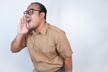a man Asian civil servants or state civil servants is with brown uniform. gesture shouting and screaming loud with a hand on her mouth. On white background. Indonesia PNS, ASNの写真素材
