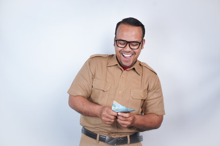 a man Asian civil servants or state civil servants is with brown uniform. gesturing happy to get money, get salary, receive taxes . On white background. Indonesia PNS, ASNの写真素材