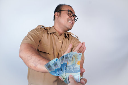 a man Asian civil servants or state civil servants is with brown uniform. gesturing take bribes. money, taking bribe from man under table. On white background. Indonesia PNS, ASNの写真素材