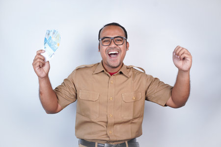 a man Asian civil servants or state civil servants is with brown uniform. gesturing happy to get money, get salary, receive taxes . On white background. Indonesia PNS, ASNの写真素材