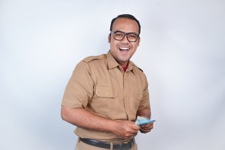 a man Asian civil servants or state civil servants is with brown uniform. gesturing happy to get money, get salary, receive taxes . On white background. Indonesia PNS, ASNの写真素材