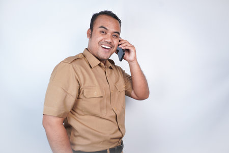 a man Asian civil servants or state civil servants is with brown uniform gesture having fun on the phone . On white background. Indonesia PNS, ASNの写真素材