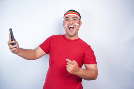 A happy Asian men wearing headband, holding his phone, and pointing copy space beside her, isolated by white background. Indonesia's independence day. indonesia menの写真素材