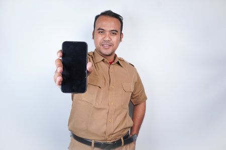 a man smiling Asian civil servants or state civil servants is with brown uniform gesture showing his phone . On white background. Indonesia PNS, ASNの写真素材