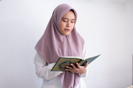 young muslim asian woman wearing a purple hijab reading a Quran. She is smiling and she is enjoying...