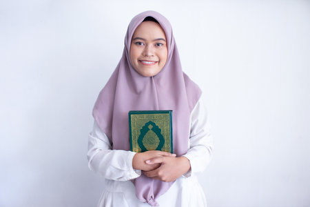 young muslim asian woman wearing a purple hijab holding a Quran. She is smiling and she is happy. Isolated on white backgroundの写真素材