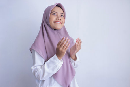 young muslim asian woman wearing a purple hijab, scarf praying. The scarf is long and covers her...
