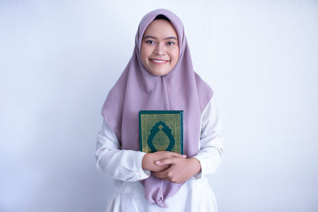 young muslim asian woman wearing a purple hijab holding a Quran. She is smiling and she is happy. Isolated on white backgroundの写真素材