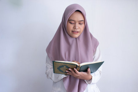 young muslim asian woman wearing a purple hijab reading a Quran. She is smiling and she is enjoying her timeの写真素材