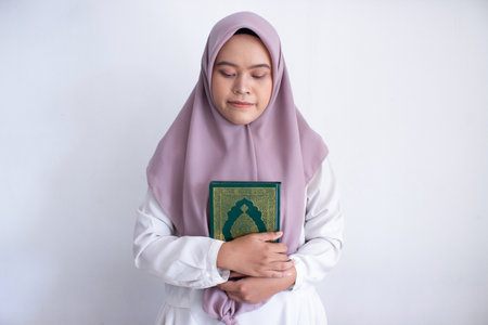 young muslim asian woman wearing a purple hijab holding a Quran. She is smiling and she is happy. Isolated on white backgroundの写真素材