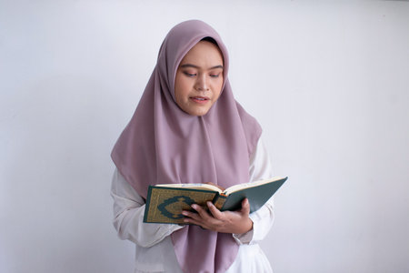 young muslim asian woman wearing a purple hijab reading a Quran. She is smiling and she is enjoying her timeの写真素材