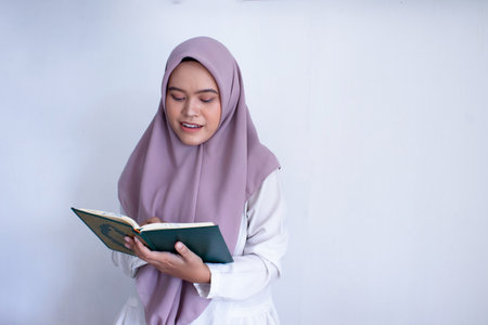 young muslim asian woman wearing a purple hijab reading a Quran. She is smiling and she is enjoying...