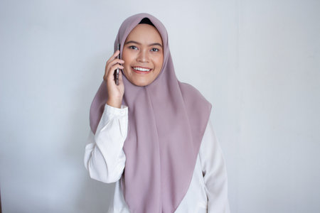 young muslim asian woman wearing a purple hijab a head scarf is talking on her cell phone. She is smiling and she is happyの写真素材