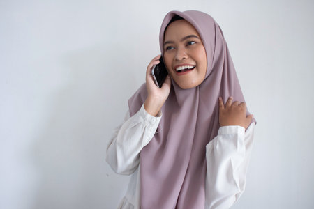 young muslim asian woman wearing a purple hijab a head scarf is talking on her cell phone. She is smiling and she is happyの写真素材
