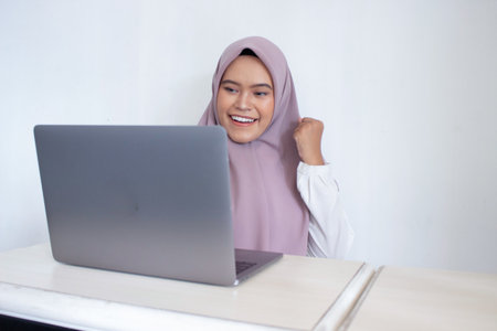 young muslim asian woman wearing a purple hijab scarf is smiling and holding her hands up in the air...