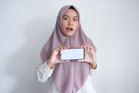 young muslim asian woman wearing a purple hijab, head scarf holding a cell phone copy space at...