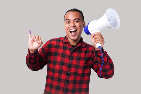 Energetic Indonesian man in flannel shirt outfit , holding and shouting at megaphone, proudly...