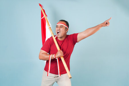 young Energetic Indonesian man is holding a flag while raising fist gesture and shouting loud,...