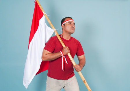 young Energetic Indonesian man is holding a flag while raising fist gesture and shouting loud,...