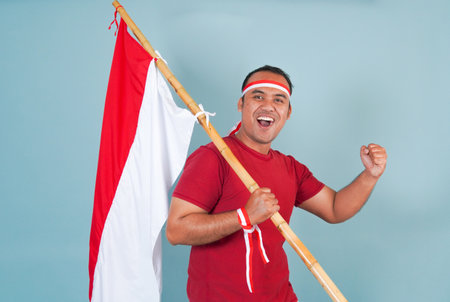 young Energetic Indonesian man is holding a flag while raising fist gesture and shouting loud, Indonesia Independence Day concept.の写真素材