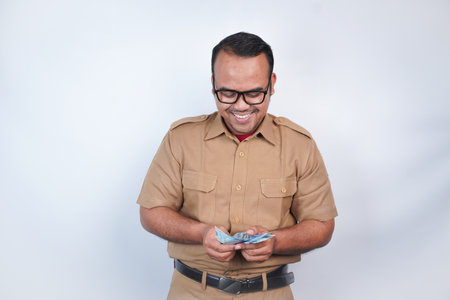 a man Asian civil servants or state civil servants is with brown uniform. gesturing happy to get money, get salary, receive taxes . On white background. Indonesia PNS, ASNの写真素材