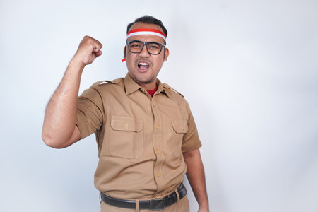 a man Asian civil servants or state civil servants is with brown uniform and red and white Headband gesture happy successful expression, raised a fist beside him On white background. Indonesia PNS, ASNの写真素材