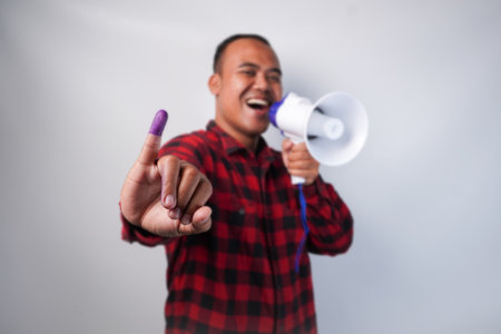 Energetic Indonesian man in flannel shirt outfit , holding and shouting at megaphone, proudly...
