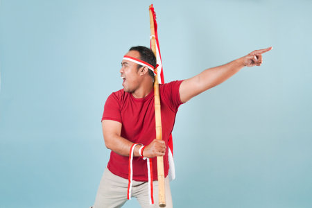 young Energetic Indonesian man is holding a flag while raising fist gesture and shouting loud, Indonesia Independence Day concept.の写真素材