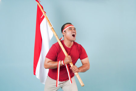 young Energetic Indonesian man is holding a flag while raising fist gesture and shouting loud, Indonesia Independence Day concept.の写真素材