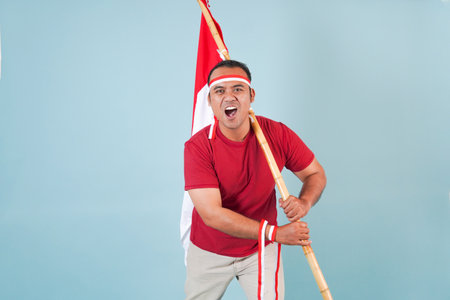 young Energetic Indonesian man is holding a flag while raising fist gesture and shouting loud, Indonesia Independence Day concept.の写真素材