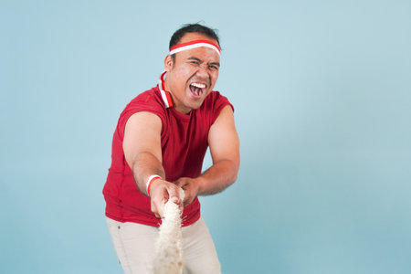 a man Indonesian wearing flag headband are pulling on a rope, joining competition for Indonesian Independence Day. Scene is lighthearted and fun.の写真素材